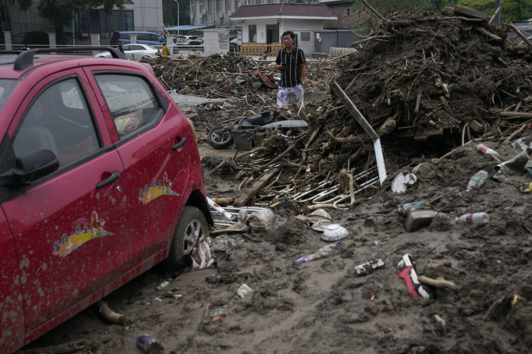 En man går igenom bråten efter kraftiga regn i områden utanför Peking.