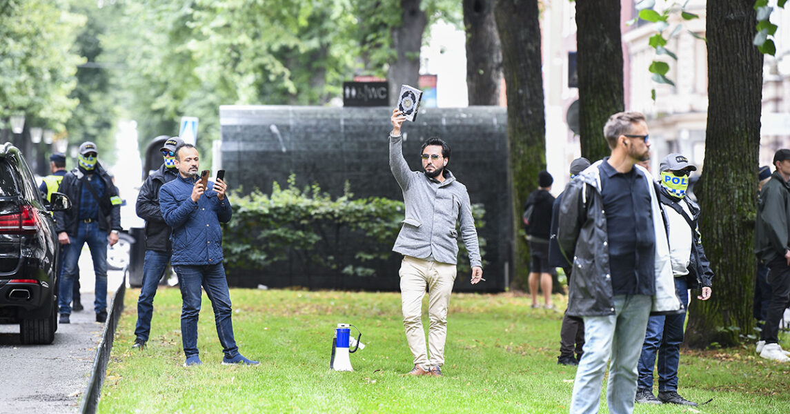 Skyddad av polis visar Salwan Momika upp det exemplar av Koranen som han sedan brände utanför den pakistanska ambassaden i Stockholm den 28 augusti.