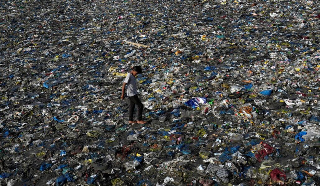 En pojke går runt i ett hav av plast vid en strand i den indiska staden Bombay.