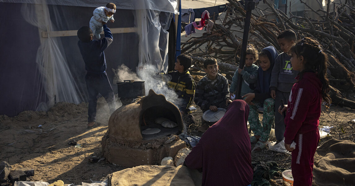 Barn som tvingats fly sina hem väntar på att maten ska bli klar i ett provisoriskt tältläger i Gaza.