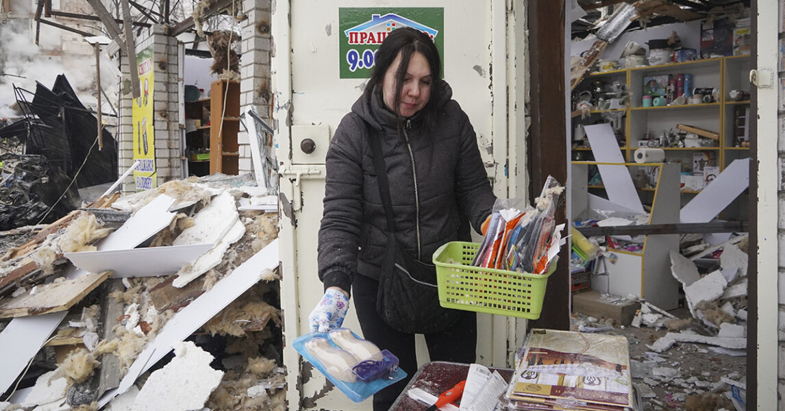 En försäljare räddar det som räddas kan från sin butik i Charkiv efter ett raketanfall den 23 januari.