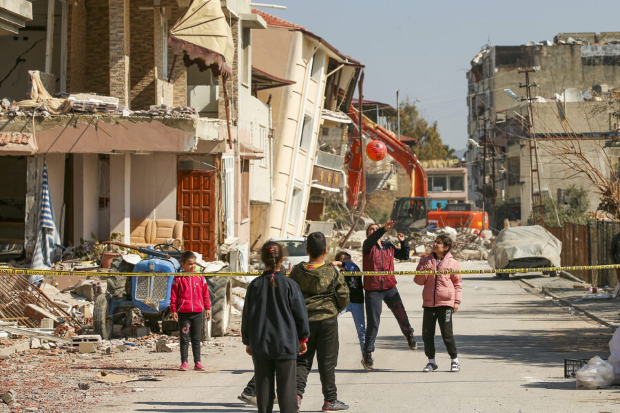 Barn leker bredvid förstörda byggnader i den turkiska staden Samandag den 22 februari 2023.