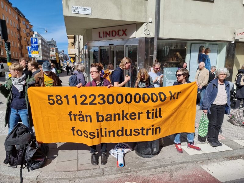 Personer demonstrerar på en gata med en banner med texten 58112230000000 kronor från banker till fossilindustrin.