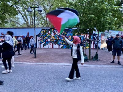 Flicka med palestinasjal och -flagga i demonstrationståg.