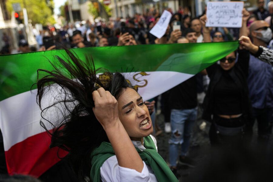 Kvinna med knuten näve i folkmassa med Irans flagga.