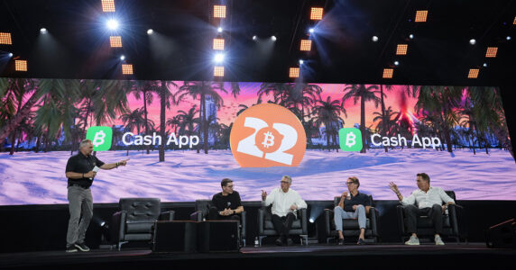 Män på en scen med bitcoin-symboler.