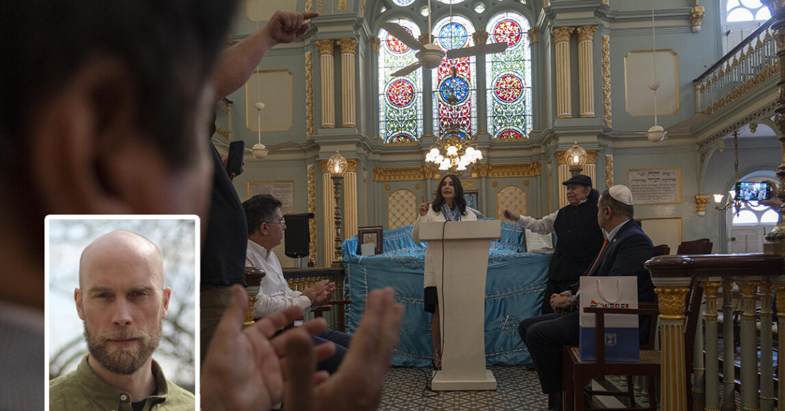 En kvinna står i en synagoga och talar till en grupp män. En av dem applåderar.