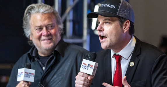 Trumps före detta rådgivare Steve Bannon tittar på republikanen Matt Gatz och ler. Gaetz talar i en mikrofon och har en keps på sig.