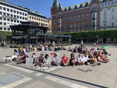 Mammor och barn sitter i en cirkel på ett torg.