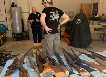 Två män, en civilist och en polis, står bland vapen som ligger på golvet