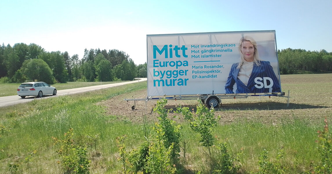 På en trailer på en åker vid en väg står Sverigedemokraternas valplakat.