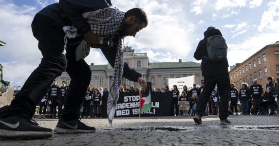 En man med palestinasjal rättar till en palestinsk flagga som står på marken. Bakom honom står folk med plakat.