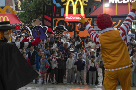 Barn tittar på mcdonaldsmaskot uppträda nära en attraktion som marknadsför den västerländska snabbmatskedjan McDonald's i Peking, lördagen den 25 maj 2024. (AP Photo/Ng Han Guan)