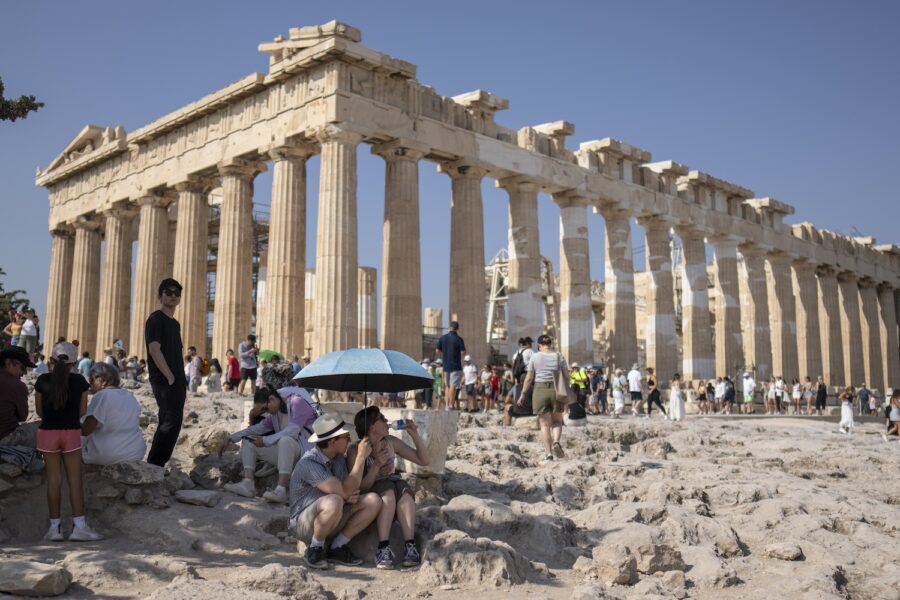 Akropolis och turister som tar skydd från solen under ett paraply.