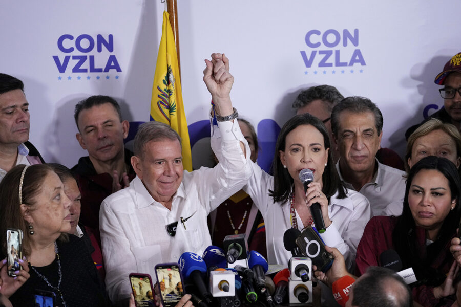 Oppositionsledarna Edmundo González och María Corina Machado håller nävarna i luften på presskonferens..