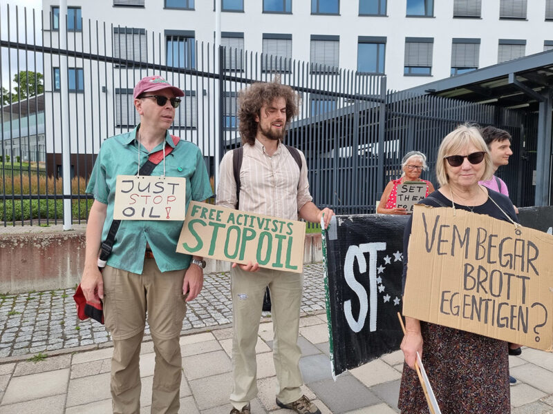 Demonstranter framför stängsel, på skyltar: Just stop oil, Free activists, Vem begår brott egentligen?