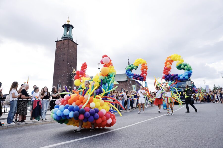 Prideparad med klänning med ballonger i regnbågens färger.