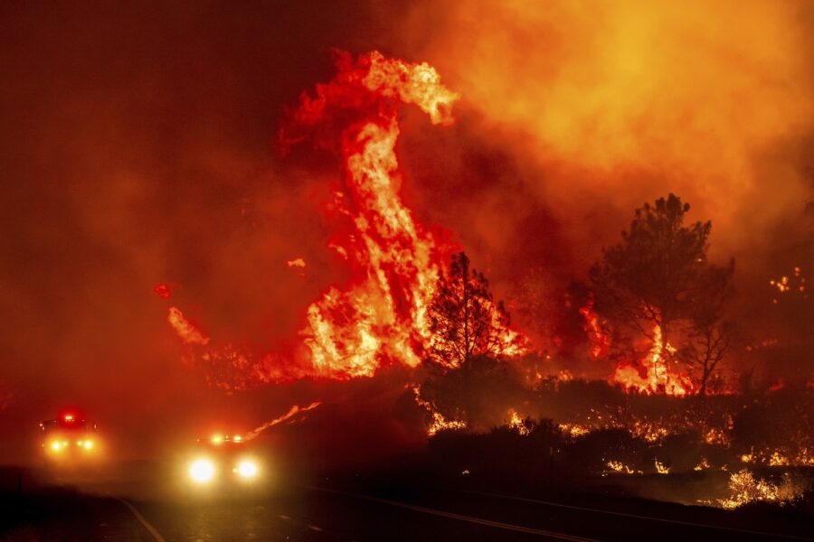 Stora flammor längs en väg med två bilar.