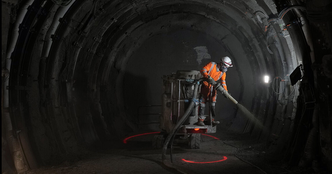 En arbetare sprutar cement i en mörk tunnel.