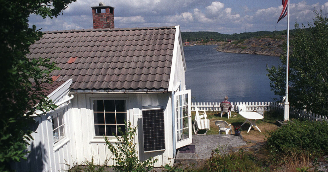 Solpanel på ett vitt hus på en höjd vid en fjord.