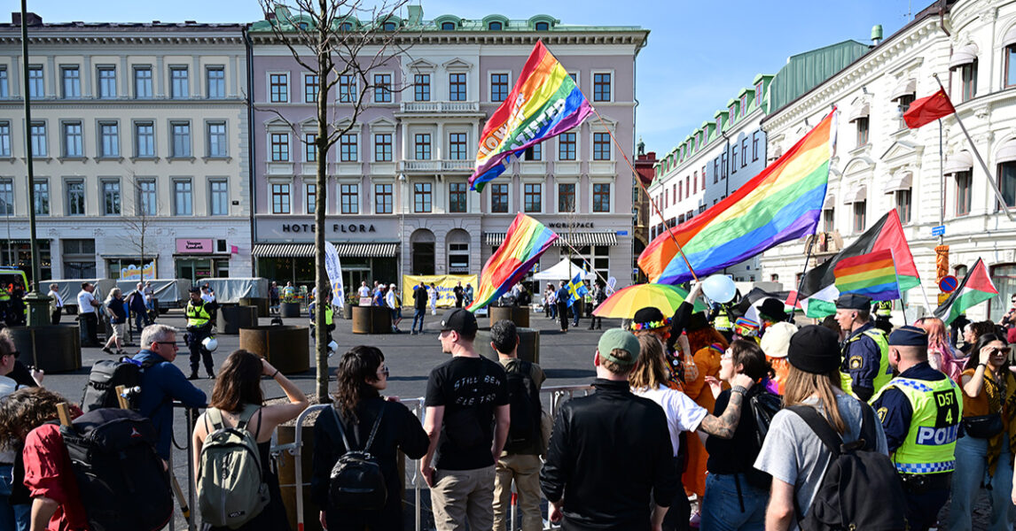 Folk med regnbågsflaggor står på ett torg och protesterar mot en nazistdemonstration.