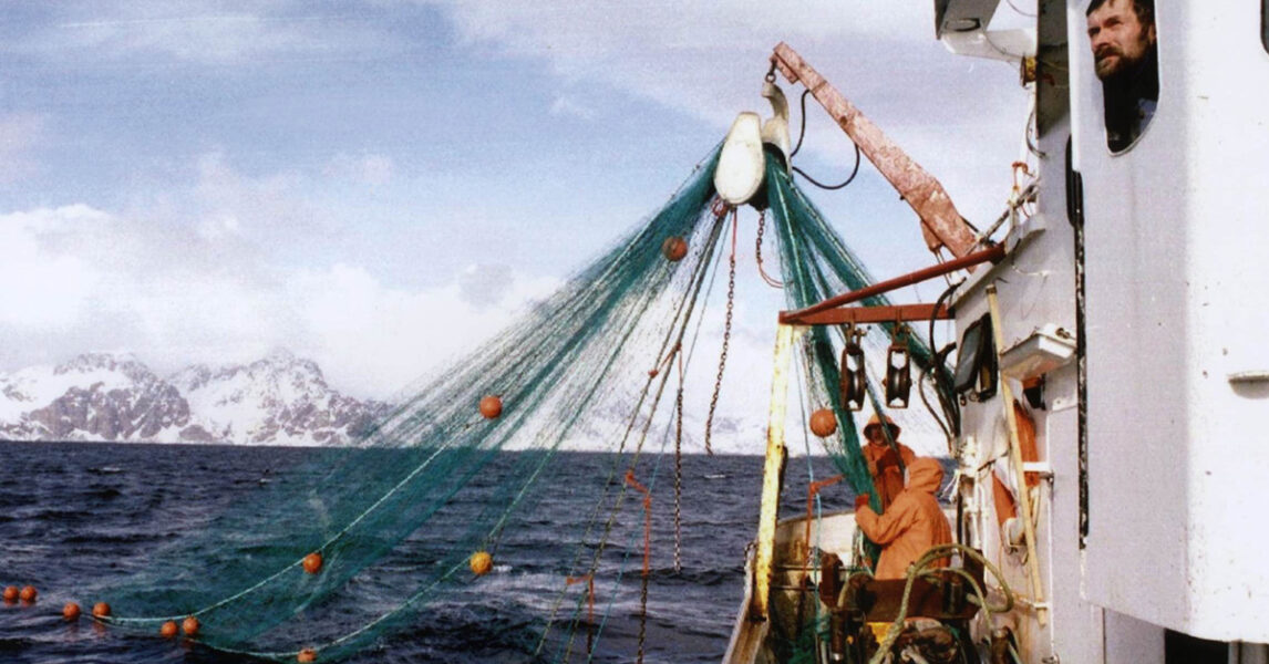 Två fiskare och fiskenät på en trålare i havet.