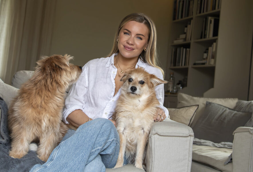 Therese Lindgren sitter i en fåtölj med två hundar.