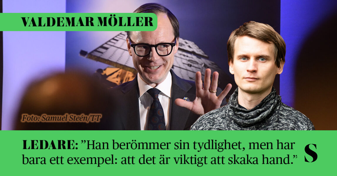 En man håller upp handen och ler stelt.