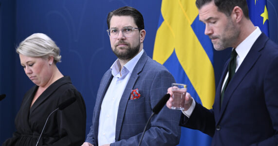 Tre politiker framför en svensk flagga.
