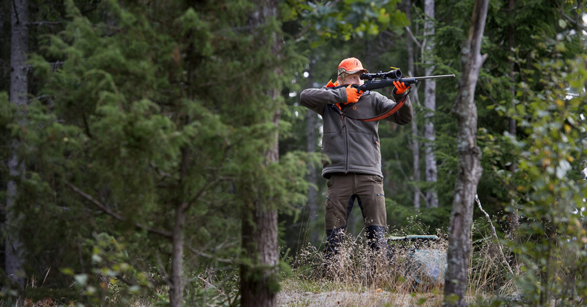 En jägare står i skogen och siktar med geväret.