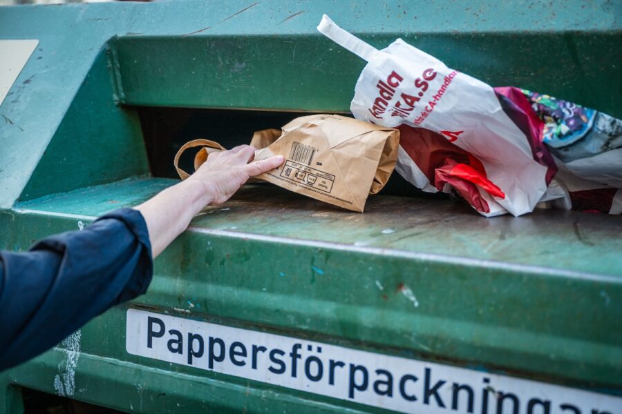 En hand lägger in en papperspåse i containern för pappersförpackningar.