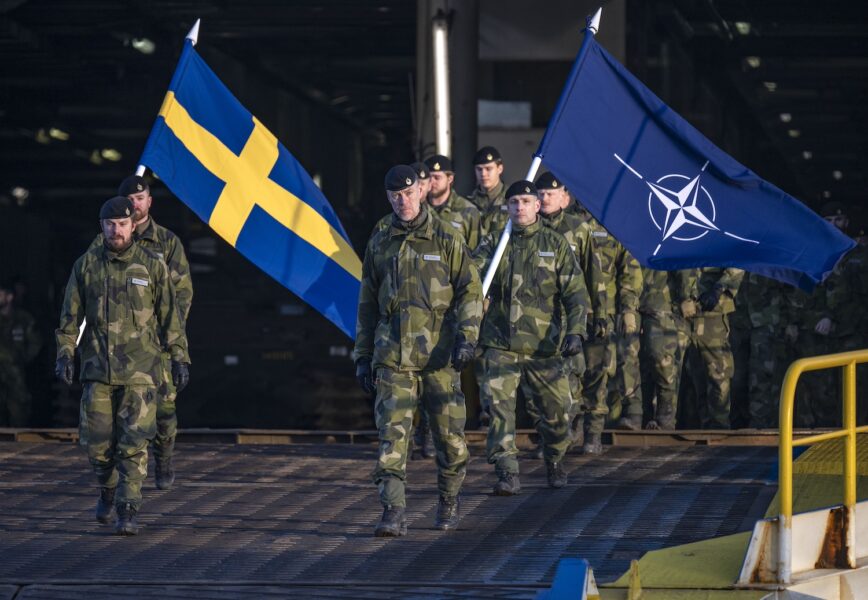 Soldater går av en färja, hållandes en svensk flagga och en Natoflagga.