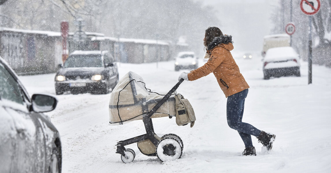 En kvinna drar en barnvagn över en snöig gata.