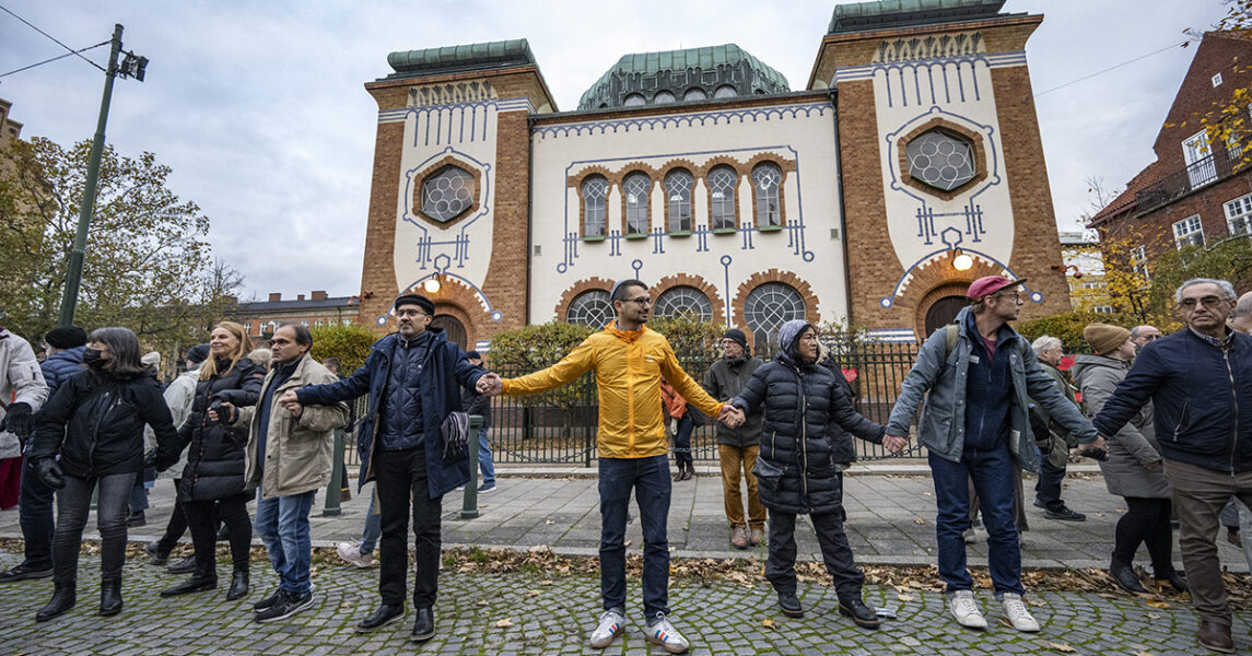 Människor står med plakat framför en synagoga.