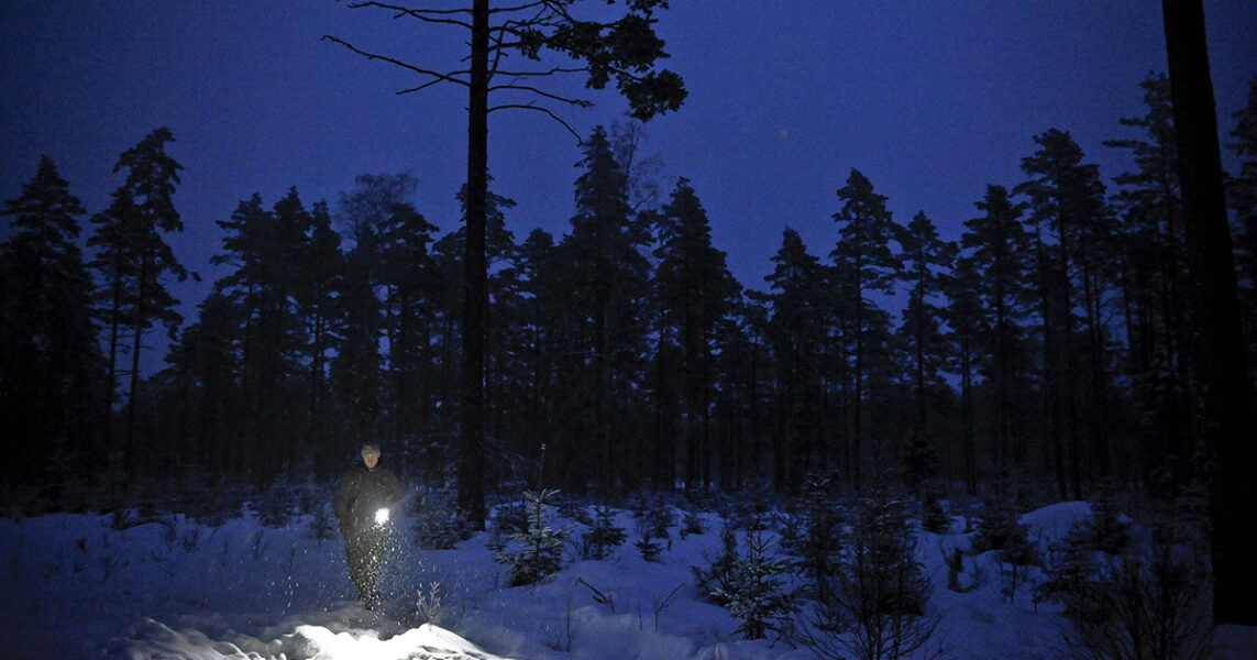 En man med ficklampa på ett hygge i snö och mörker.