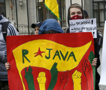 En kvinna håller upp en flagga som det står Rojava på.