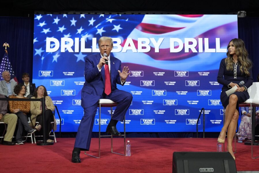 Donald Trump sitter framför en storbildsskärm där det står Drill baby drill.