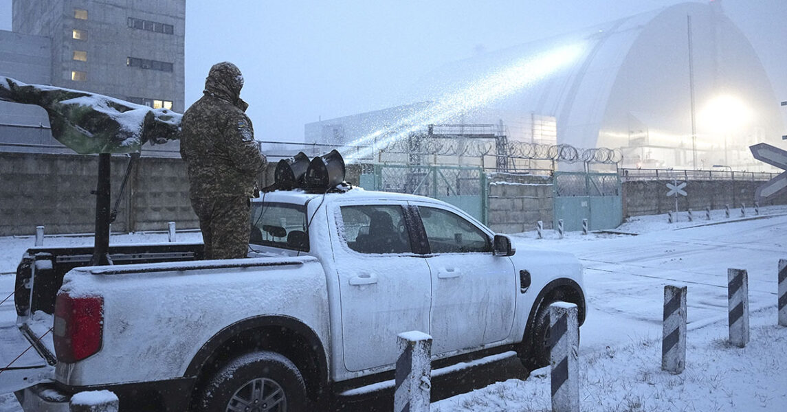 En man står på ett bilflak och siktar med ett vapen mot en stor byggnad.