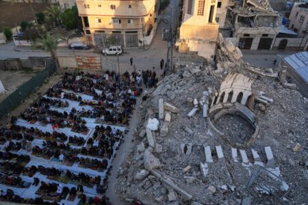 Palestinier i bönestund bredvid sönderbombade rasmassor.