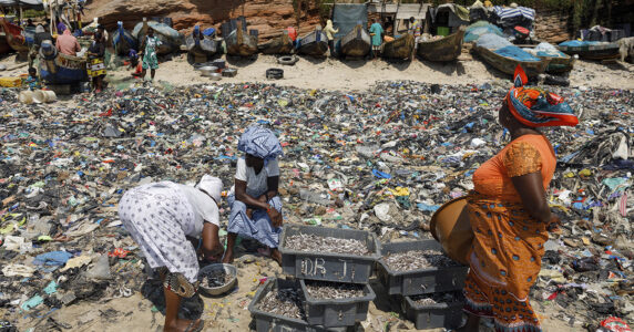 Kvinnor rensar fisk bland textilavfall.