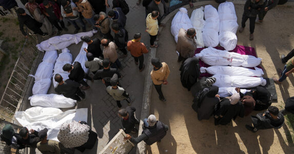 Döda människor insvepta i vitt tyg, och män som står bland dem.