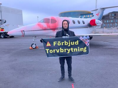 Man framför nedsprejat flygplan håller upp skylt "förbjud torvbrytning"