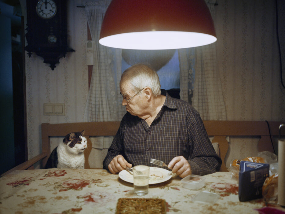 en katt och en äldre man i en kökssoffa tittar på varandra