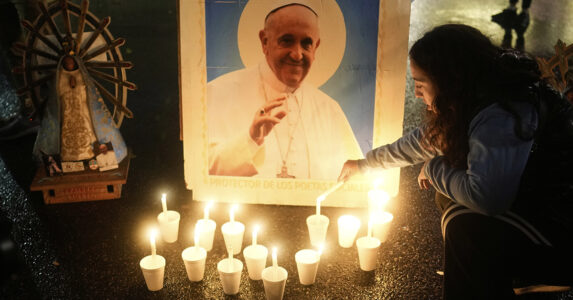 En kvinna tänder ljus framför en bild av påven.