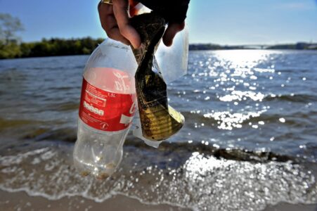 En hand håller i skräp vid stranden.