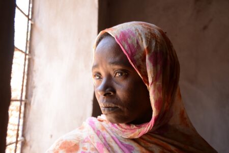 Sudanesisk kvinna tittar ut genom ett fönster.