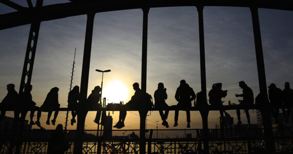 Folk på ett broräcke i solnedgång.