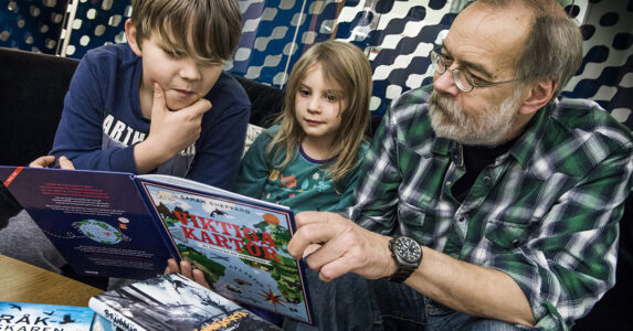 En gråhårig man läser böcker med två barn.