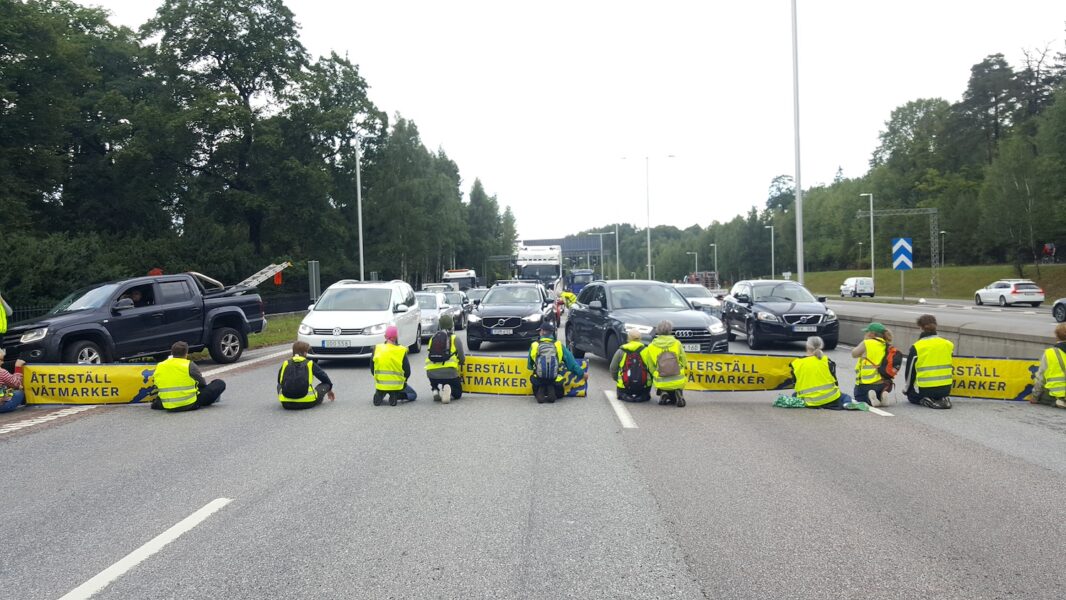 Aktivister sitter på motorvägen och blockerar bilar med banderoller med budskapet Återställ våtmarker.