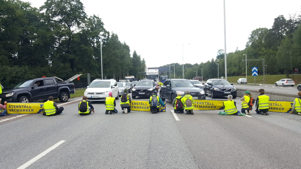 Aktivister sitter på motorvägen och blockerar bilar med banderoller med budskapet Återställ våtmarker.
